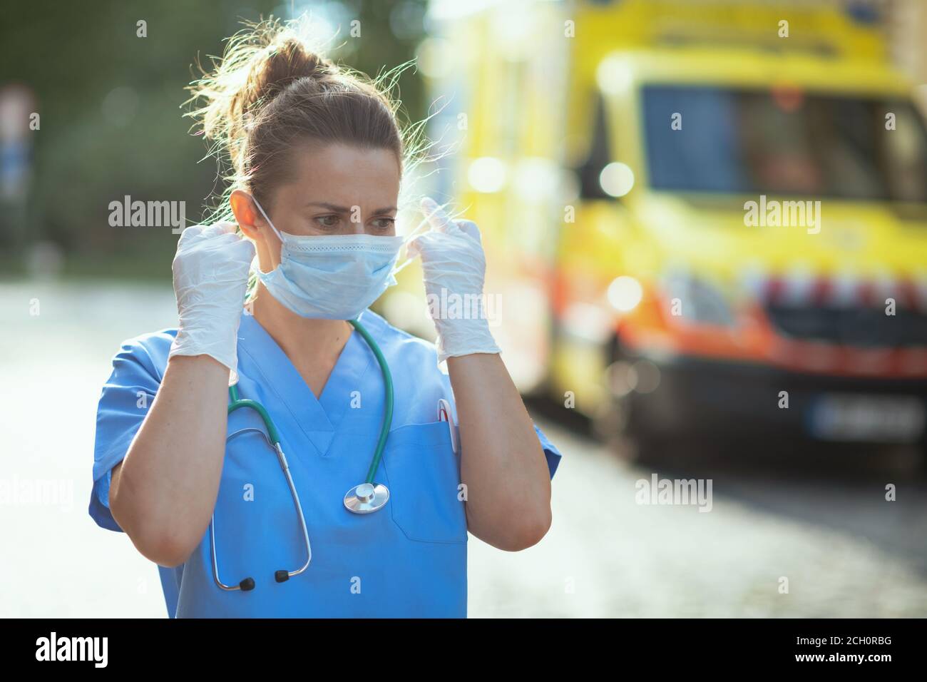 covid-19 pandemic. modern medical doctor woman in uniform with stethoscope and medical mask outside near ambulance. Stock Photo
