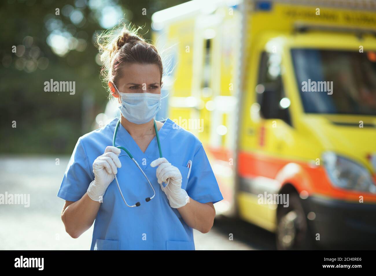 covid-19 pandemic. modern paramedic woman in scrubs with stethoscope and medical mask outside near ambulance. Stock Photo