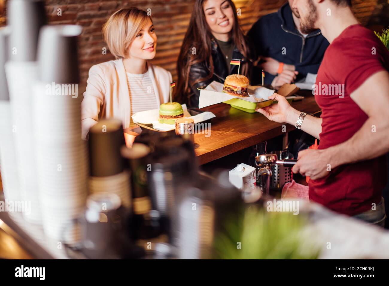 Group of happy smiling friends ordering food through barkeeper at the counter in modern restaurant with loft style, bricks and pipes, interior Stock Photo