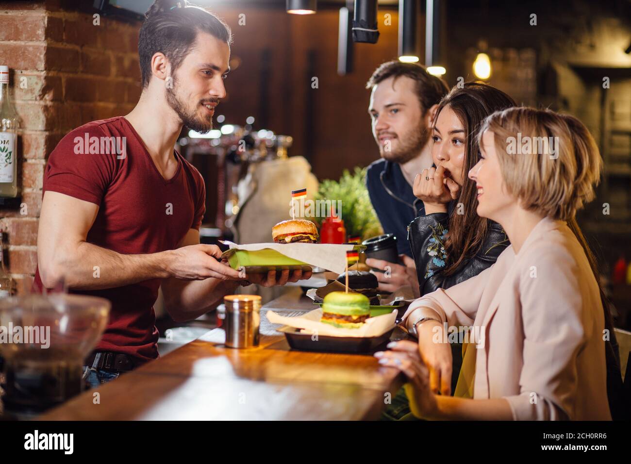 Group of happy smiling friends ordering food through barkeeper at the counter in modern restaurant with loft style, bricks and pipes, interior, Stock Photo