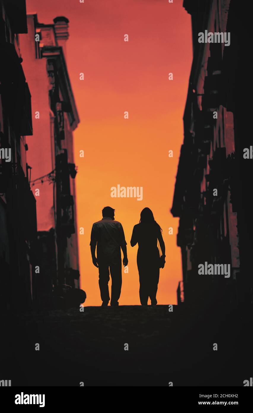 Silhouette of a man and woman walking up the road at sunset Stock Photo ...