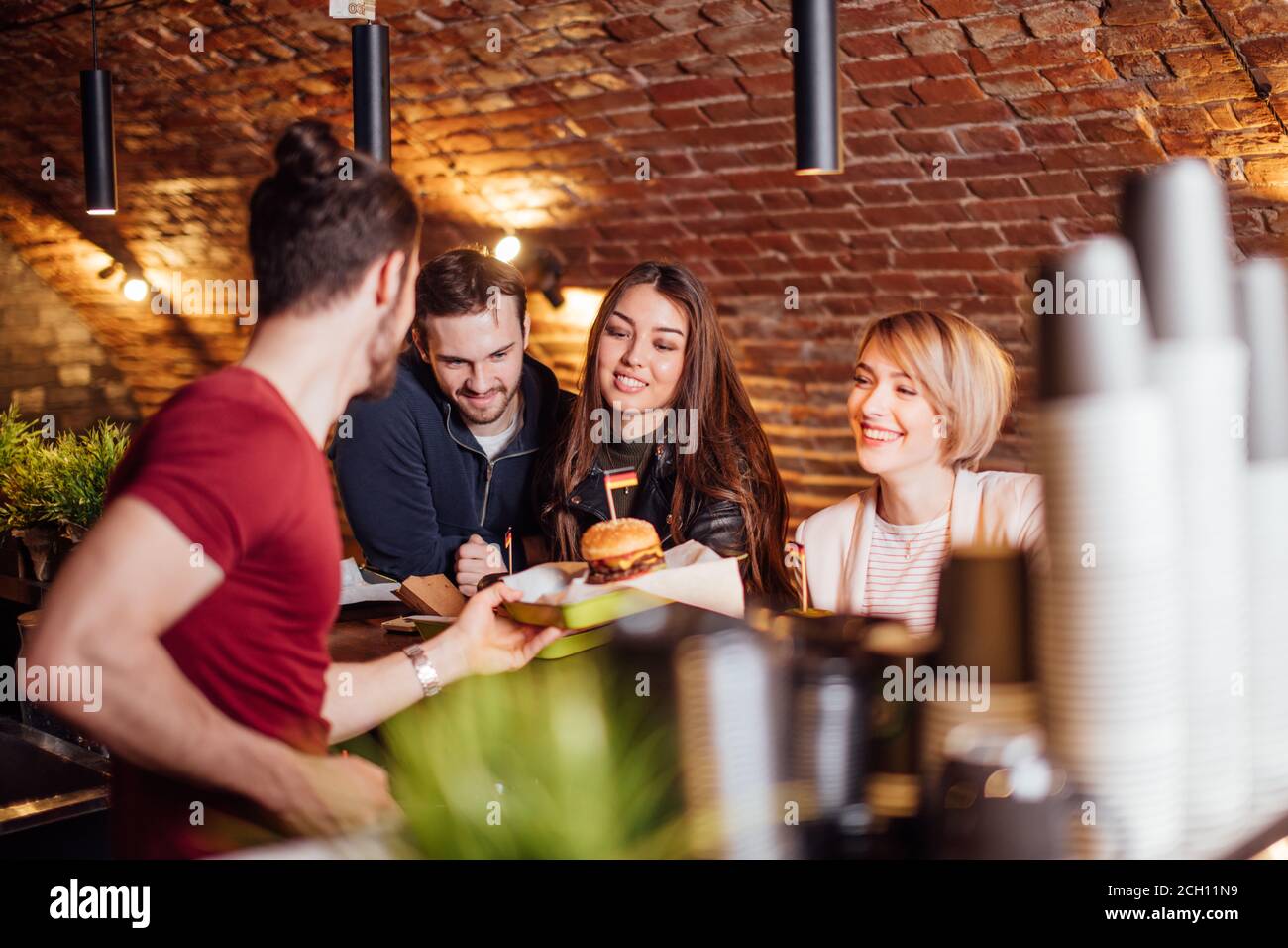 Group of happy smiling friends ordering food through barkeeper at the counter in modern restaurant with loft style, bricks and pipes, interior Stock Photo