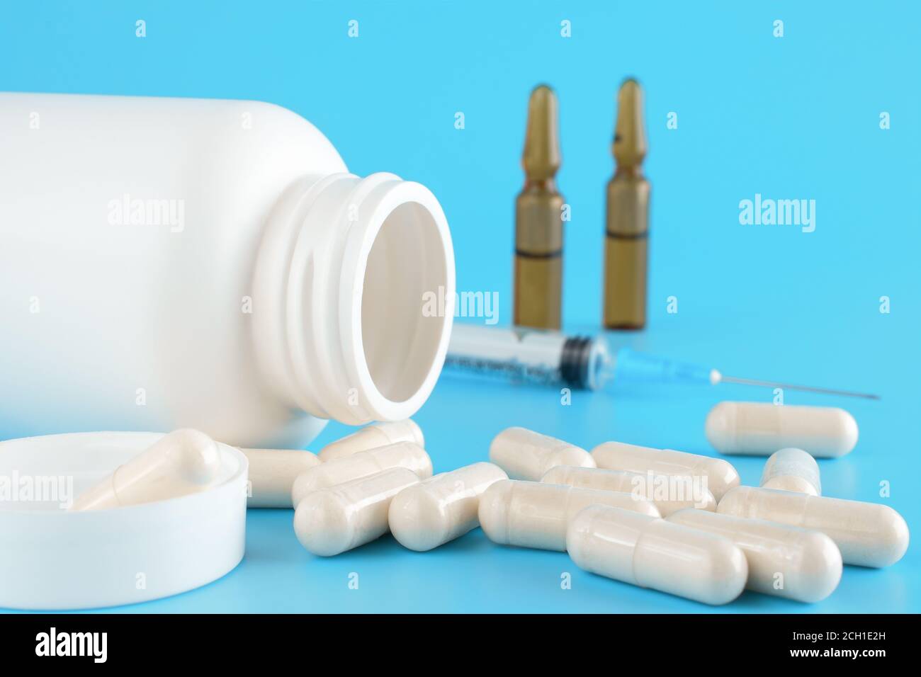 Pills, capsules, syringe, White medical containers, ampoules on blue background. Medical vial