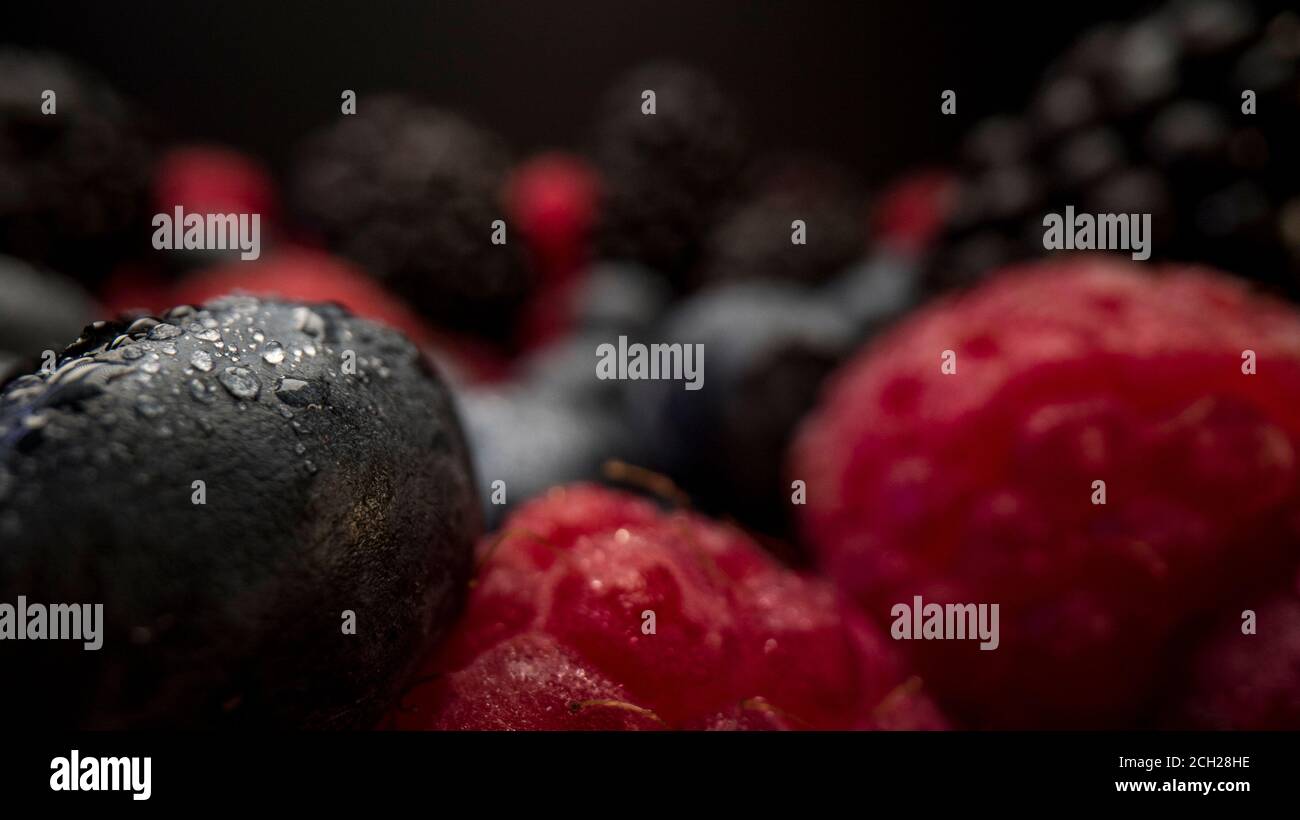 Close up view of fresh berries. Raspberries, blackberries and blueberries on black background. Tasty looking organic fruits covered with dew. Stock Photo