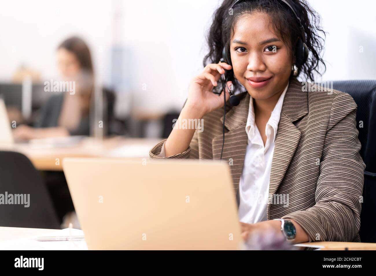 Young adult friendly confidence operator Mixed race of African and asian woman with headsets working in a call center with her colleague in background Stock Photo