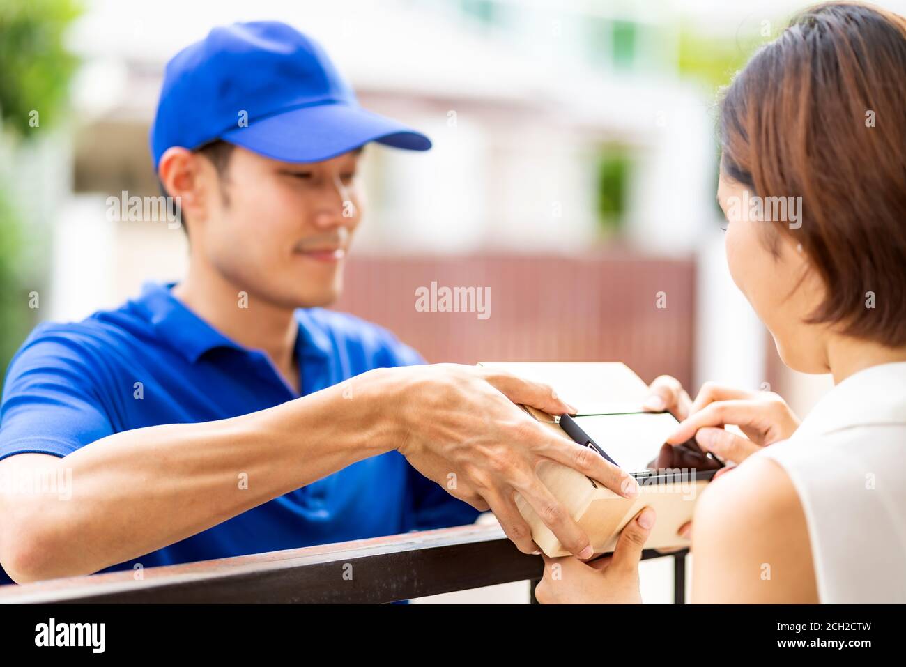 Asian woman sign electronic signature to portable mobile device after receive package from male delivery man in blue shirt. Package shopping delivery Stock Photo