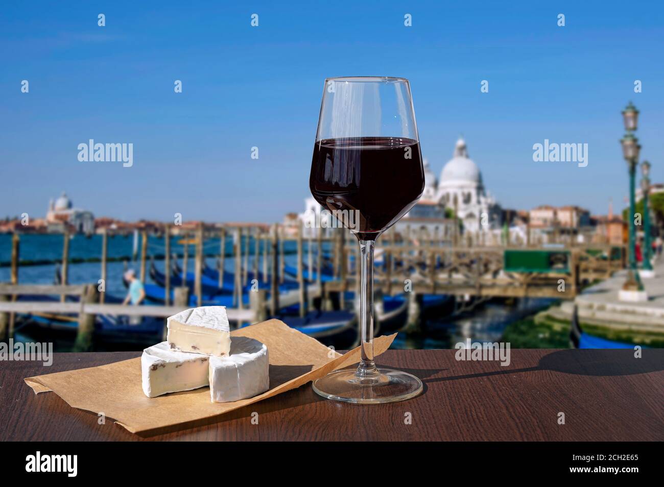 Glass of red wine with brie cheese with view on gondolas and church in Venice, Italy Stock Photo