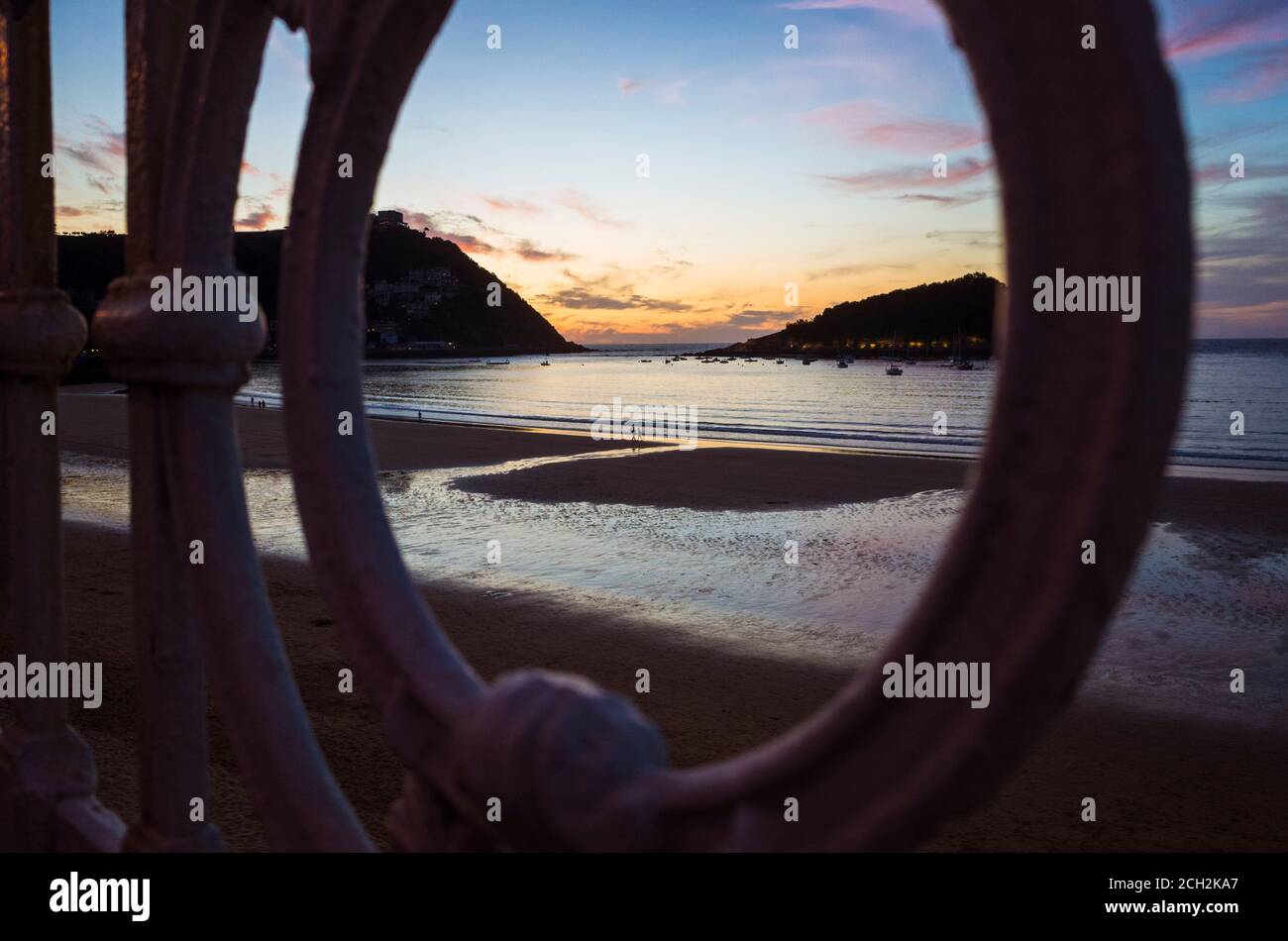 Donostia, Gipuzkoa, Basque Country, Spain - July 15th, 2019 : La Concha beach at sunset as seen through the iconic banister. Stock Photo