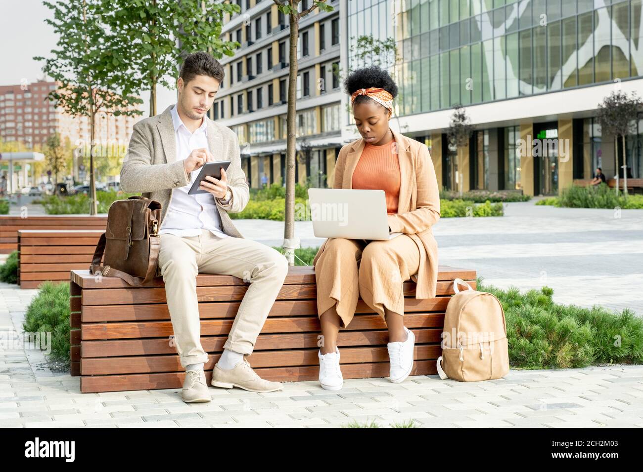 Two young contemporary intercultural co-workers using mobile gadgets Stock Photo