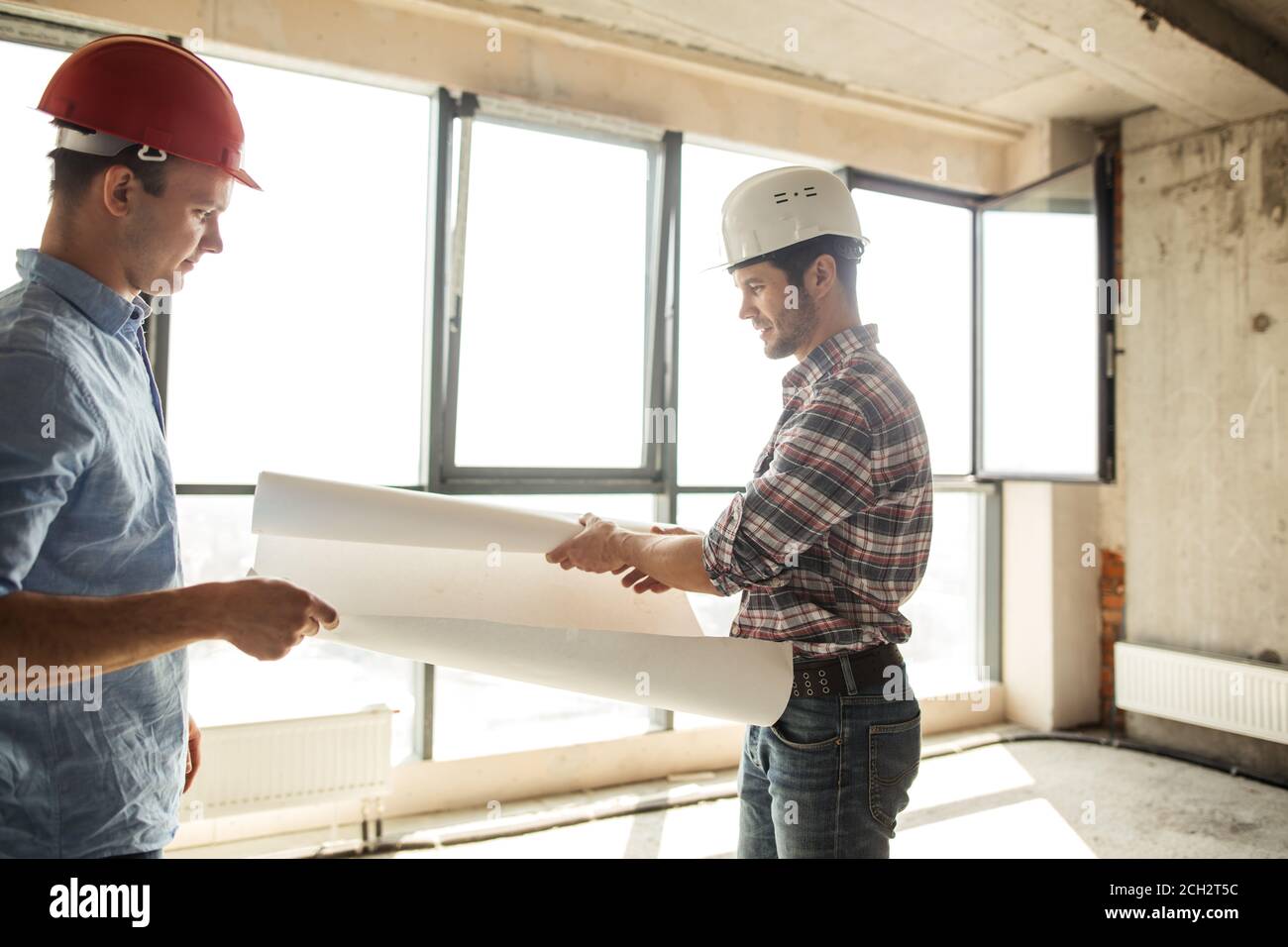 two handsome builders are unfolding a paper. paperwork in building. side view photo Stock Photo