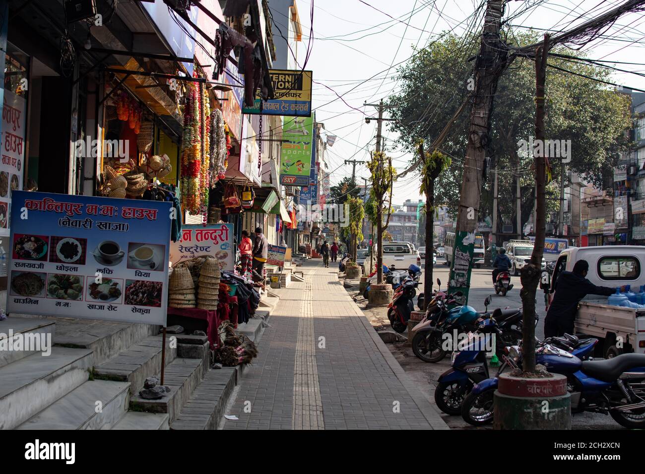 Pokhara, Nepal - December 21: Unidentified people walks on the sidewalk, enters a shop and drives a motorbike on the street Pokhara, December 2019 Stock Photo