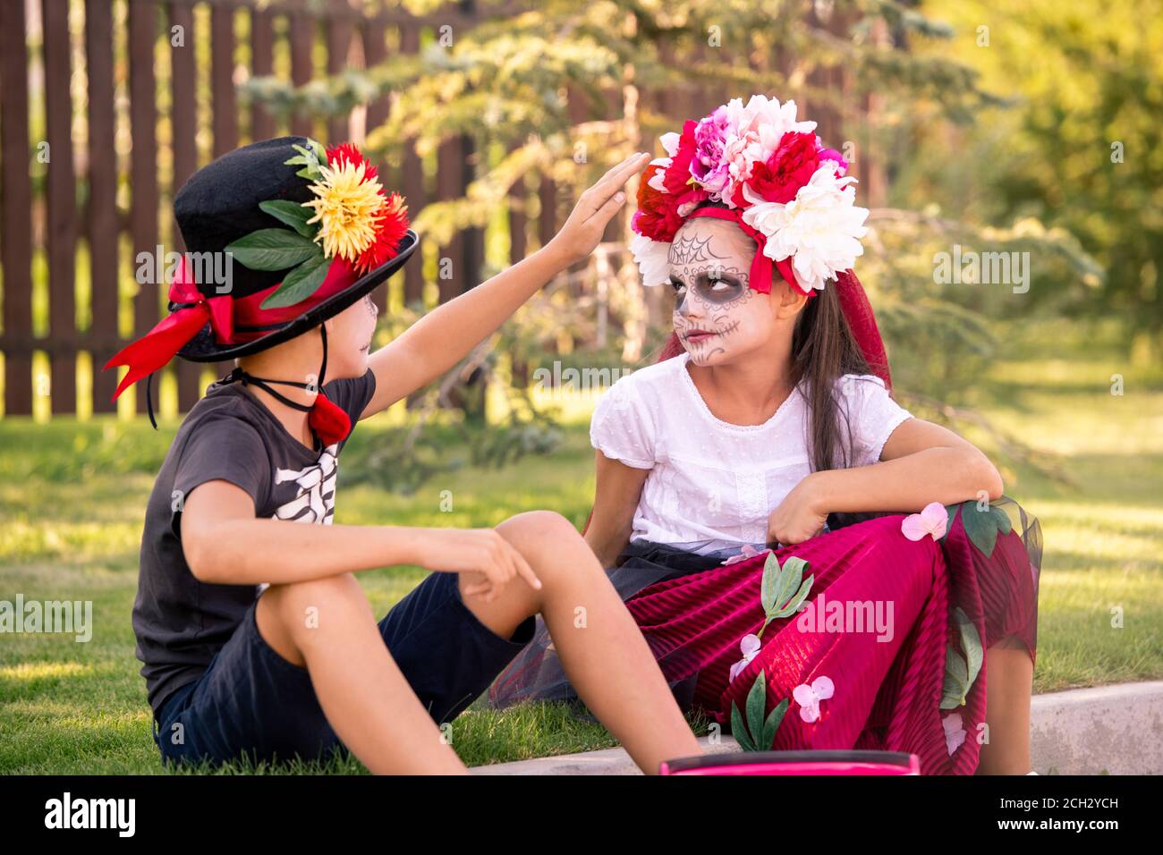 Cute boy in hat and t-shirt touching floral wreath on head of pretty girl Stock Photo