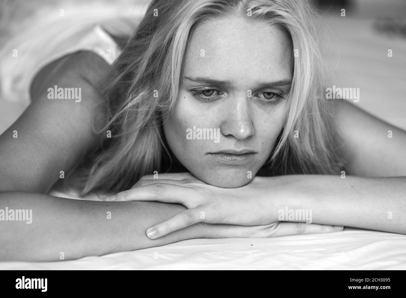 Depression and loneliness. Sad thinking young woman lying alone in bed. Black and white closeup. Stock Photo