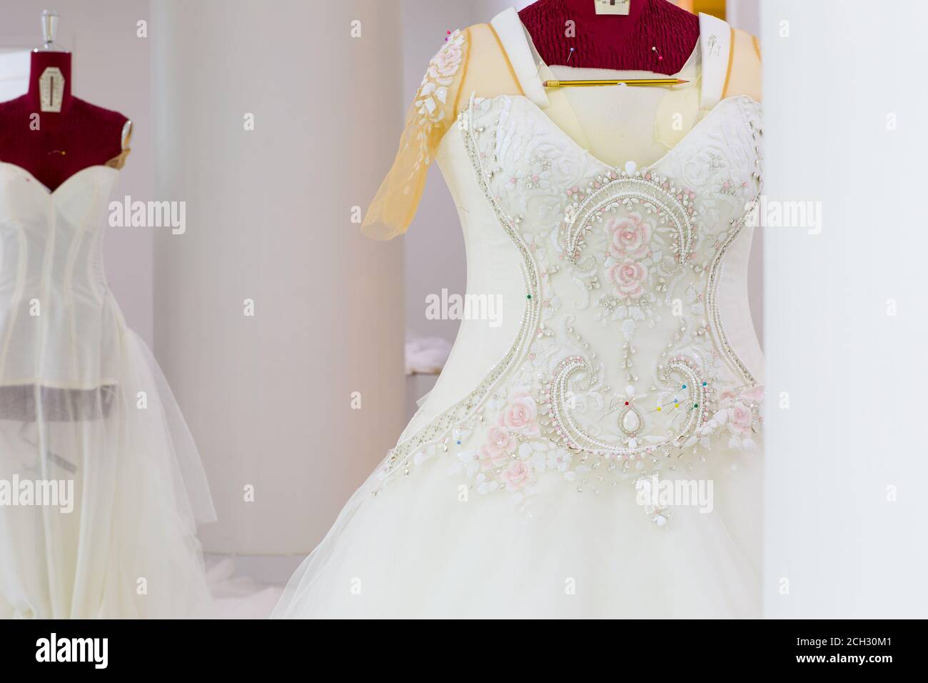 Beautiful haute-couture wedding dress with handmade intricate embroidery and crystal details on a mannequin in a bridal design workshop. Stock Photo