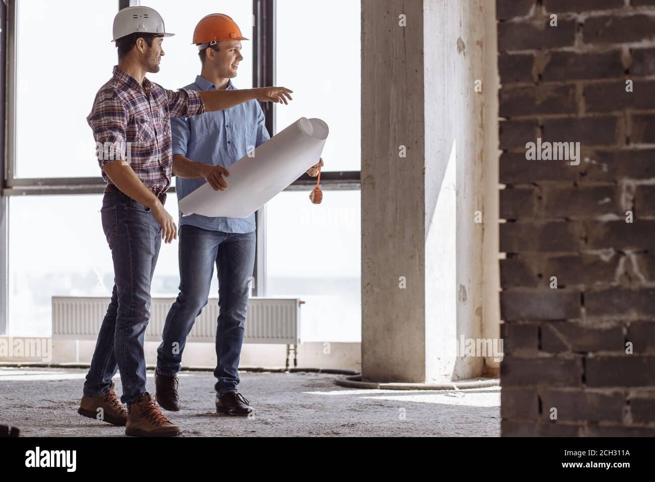 a positive engineer is boasting about new skyscraper to a colleague while walking in the construction area Stock Photo