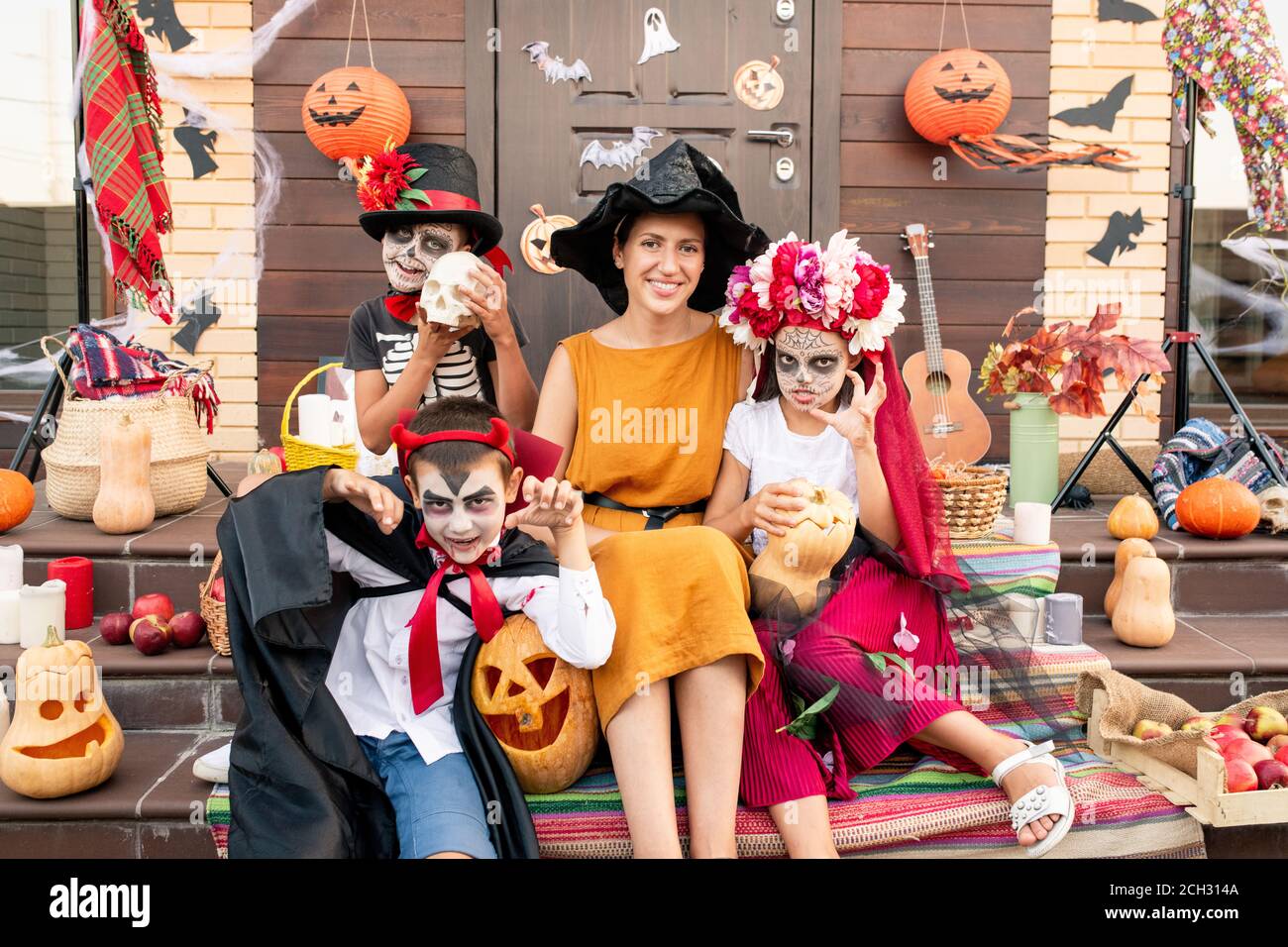 Young cheerful woman sitting on staircase among spooky halloween kids Stock Photo