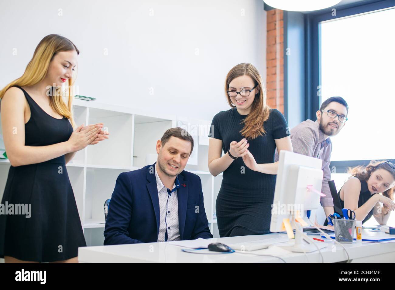 Businesswomen applauding to their modest sitting colleague. man feels confounded by colleagues' compliment Stock Photo
