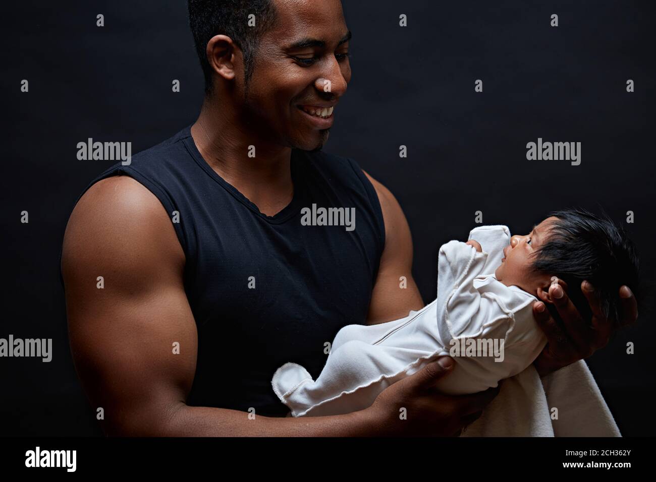 Young afro-american daddy holding his sweet newborn baby in the arms and looking at him with love. side view photo. first meeting with a adorable baby Stock Photo