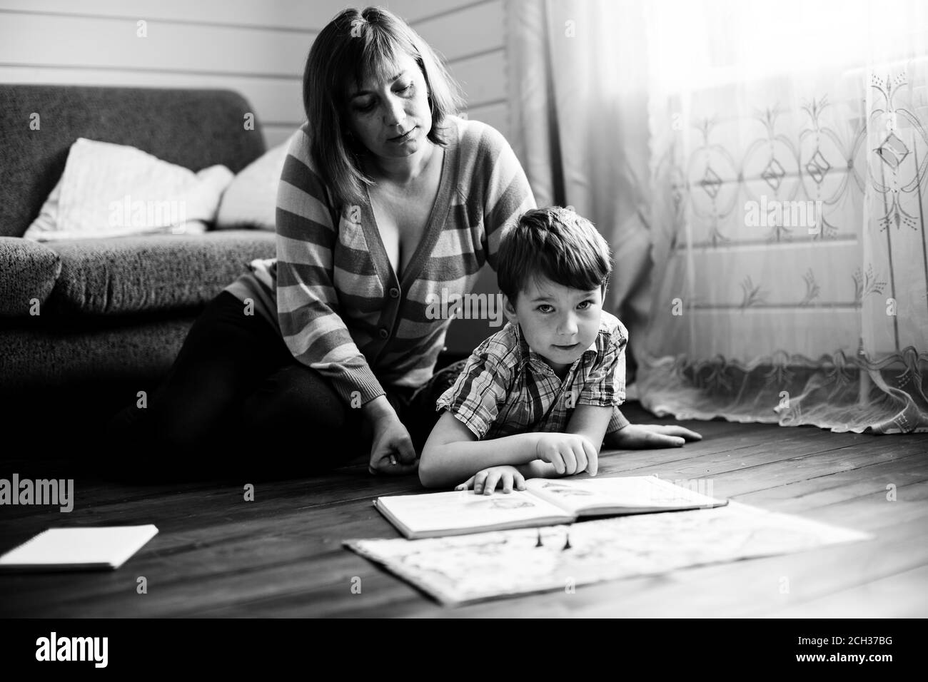 Woman reading a book with her little son on the floor in home. Black and white photo. Stock Photo