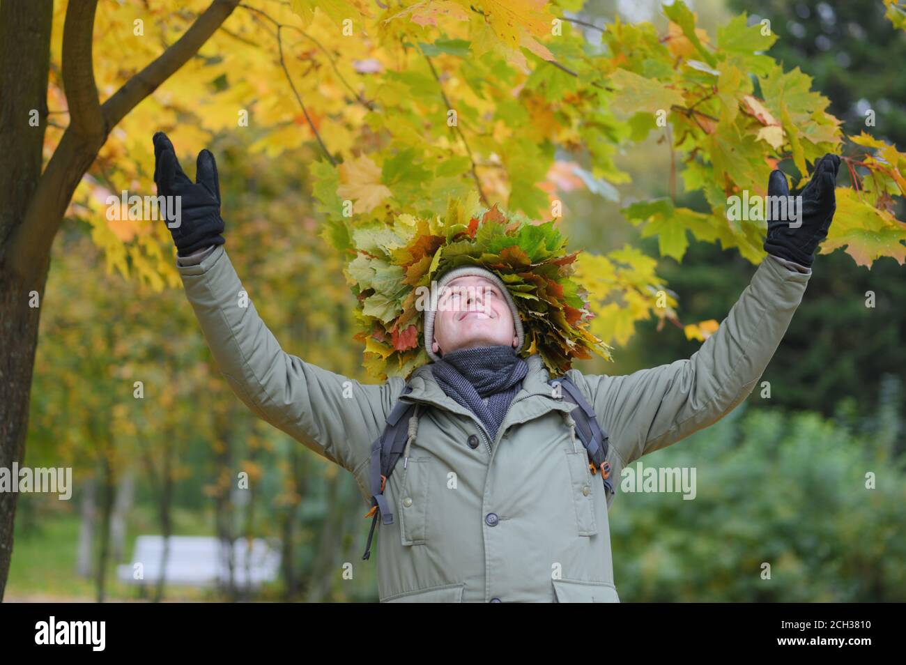 Man in autumn wreath with red and orange leaves raised his hands to the sky and looking upward Stock Photo