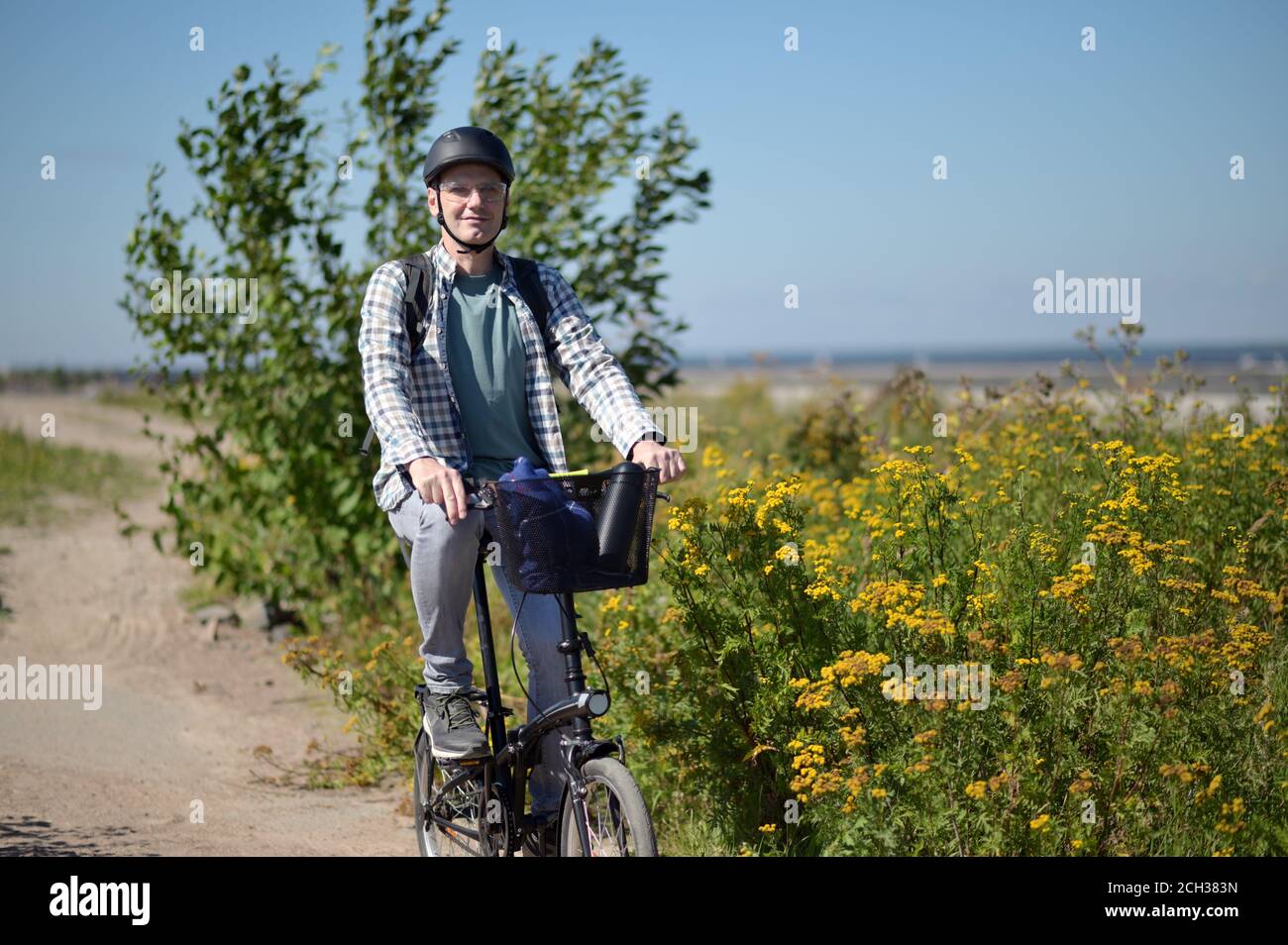 Mature Caucasian man in a bicycle helmet on his bike on the road from a beach Stock Photo