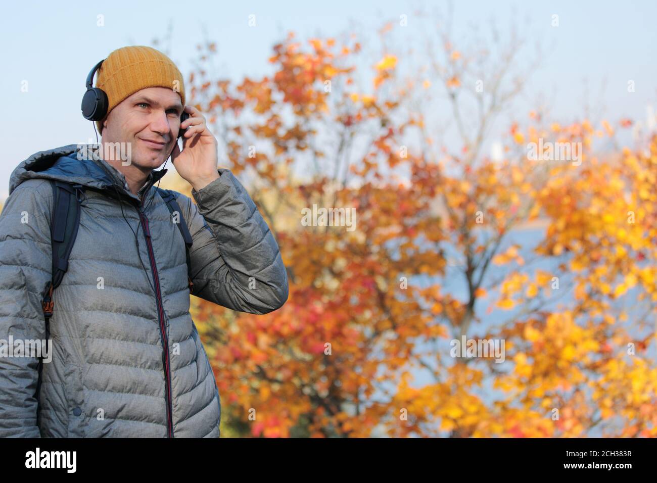 Man in headphones listening music from his smart phone outdoors in a sunny autumn day Stock Photo