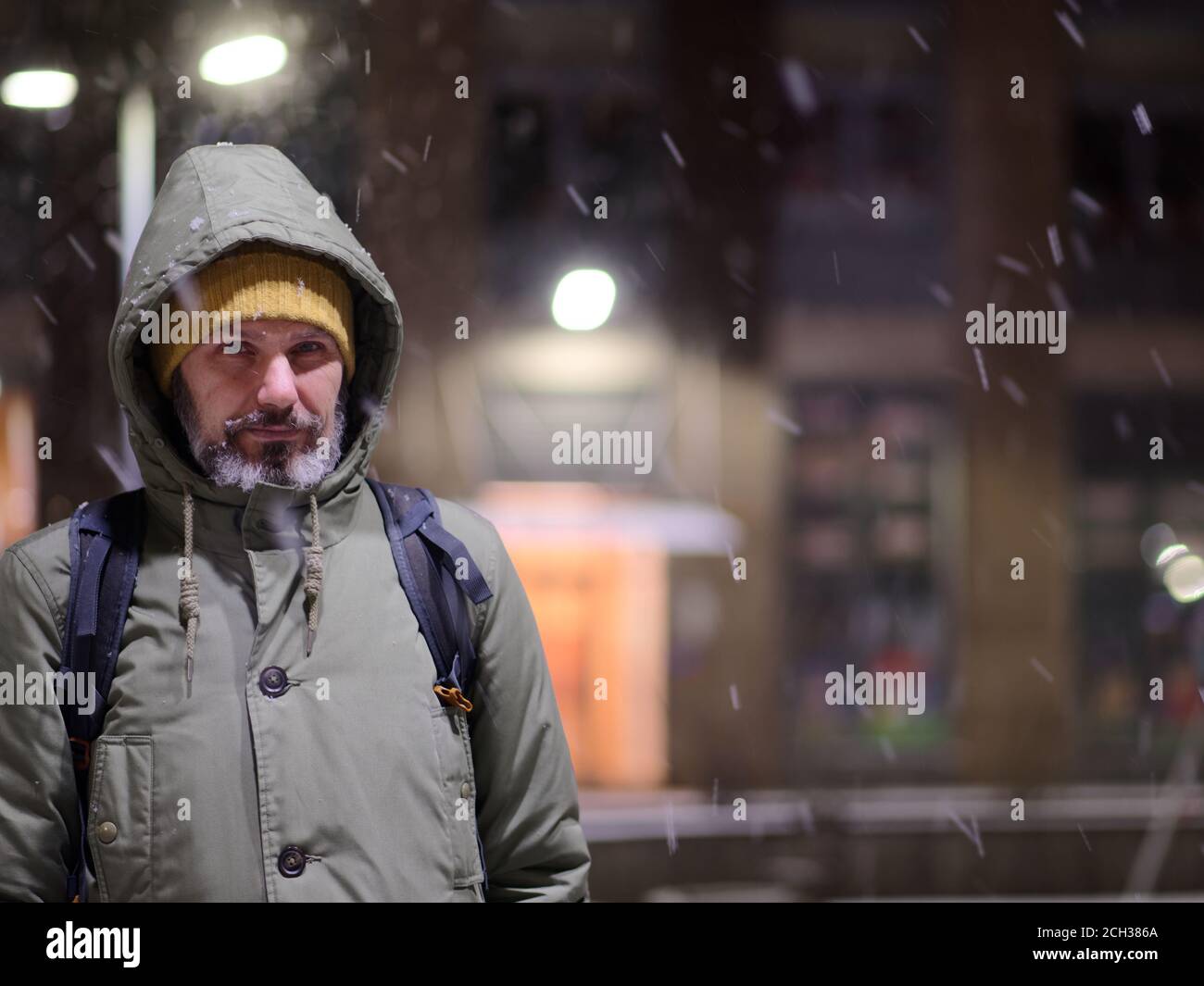 Mature Caucasian bearded man in winter jacket standing under snowfall and looking at camera Stock Photo