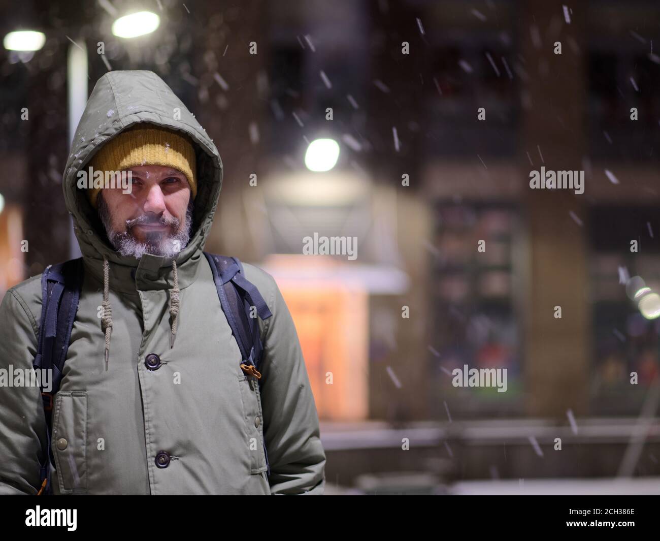 Mature Caucasian bearded man in winter jacket standing under snowfall and looking at camera Stock Photo