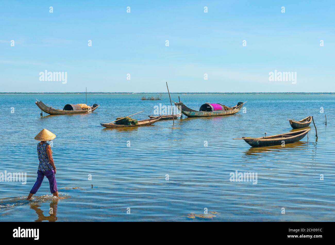 Vietnamese woman with conical hat walking towards fishing boats between Hoi An and Hue, Central Vietnam, Asia. Stock Photo