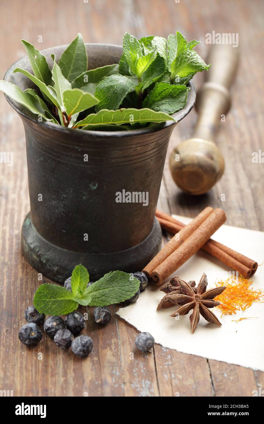 Anise, saffron, cinnamon, juniper berries and other spices in a vintage mortar on a rustic table Stock Photo