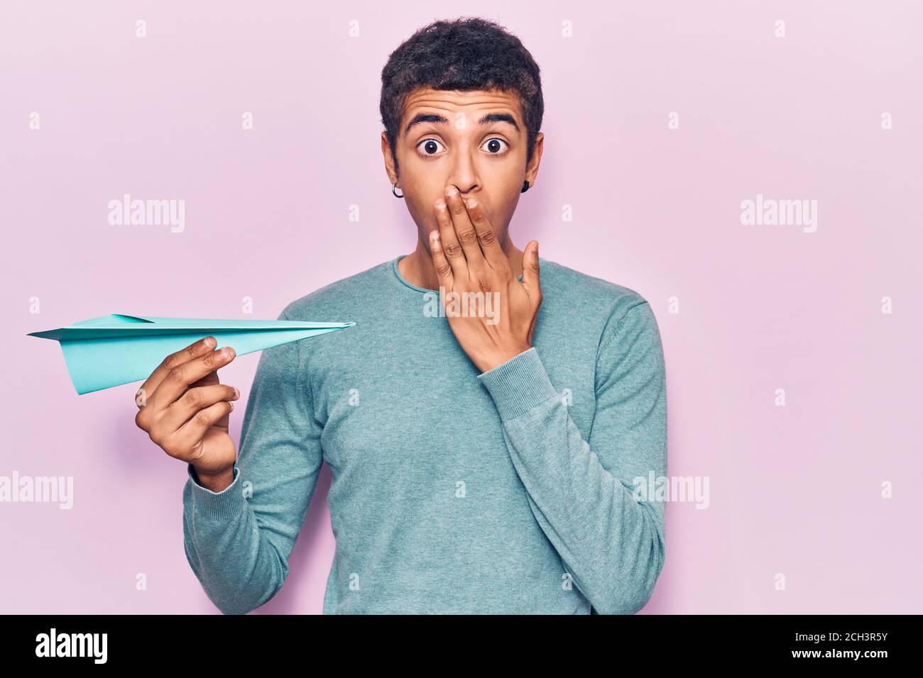 Afraid Paper Young african amercian man holding paper airplane covering mouth with ...
