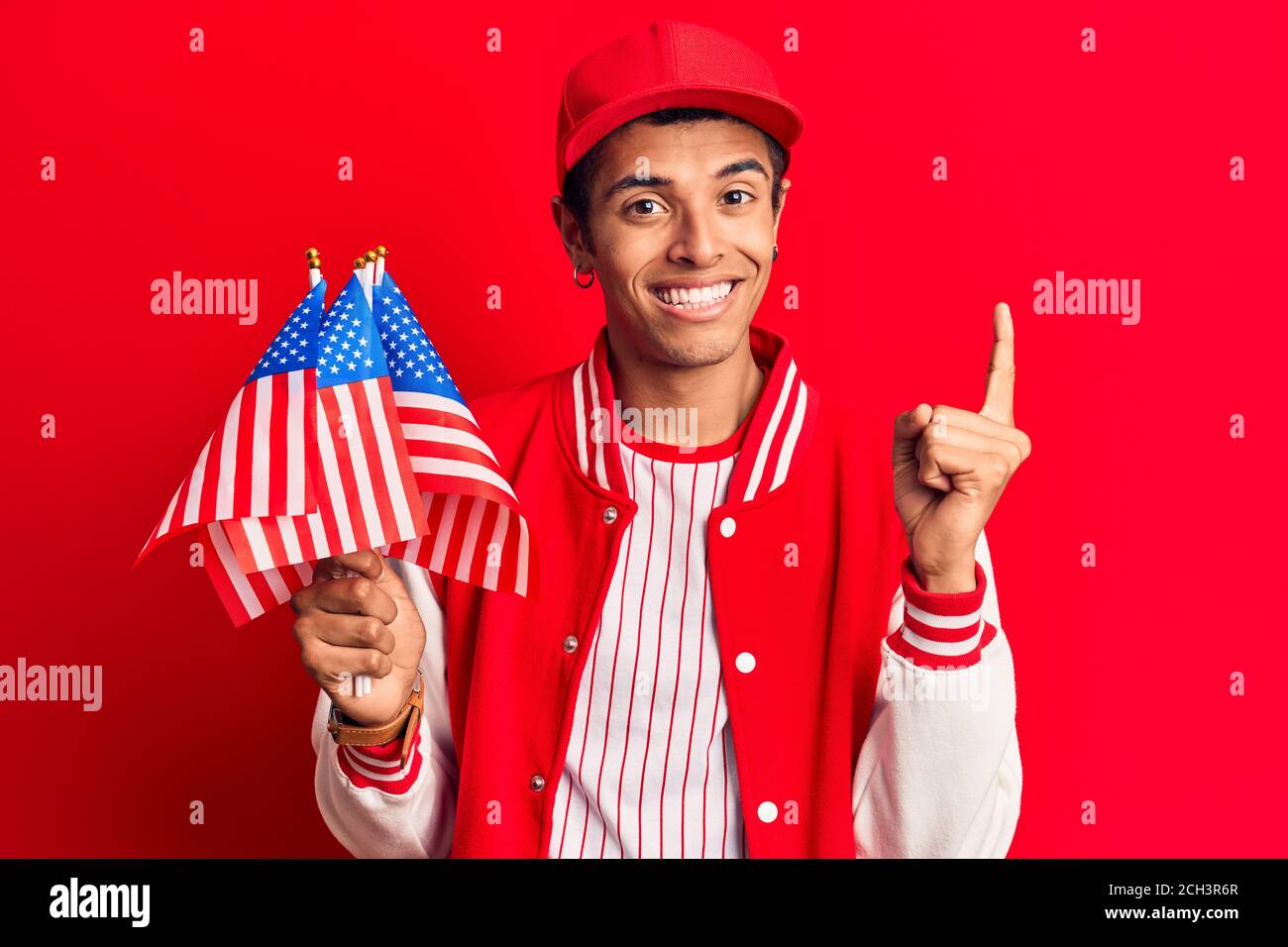 Young african amercian man wearing baseball uniform holding america flags smiling with an idea or question pointing finger with happy face, number one Stock Photo