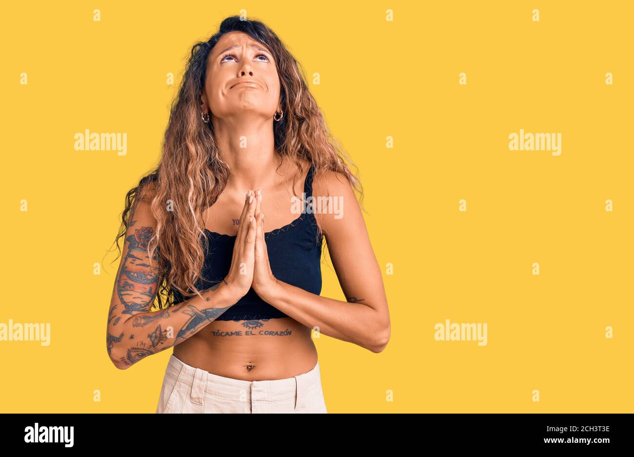 Young hispanic woman with tattoo wearing casual clothes begging and praying with hands together with hope expression on face very emotional and worrie Stock Photo
