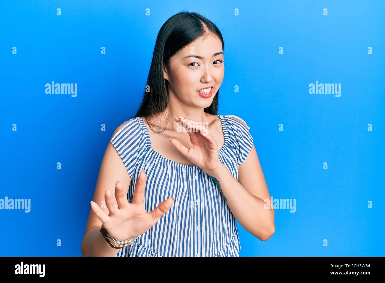 Young chinese woman wearing casual striped t-shirt disgusted expression, displeased and fearful doing disgust face because aversion reaction. with han Stock Photo