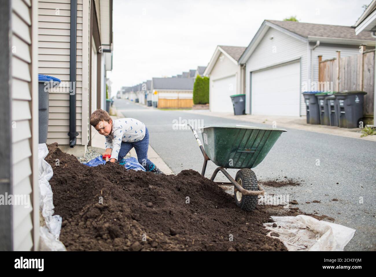 Young boy scooping pile of soil into wheelbarrow in back alley Stock ...