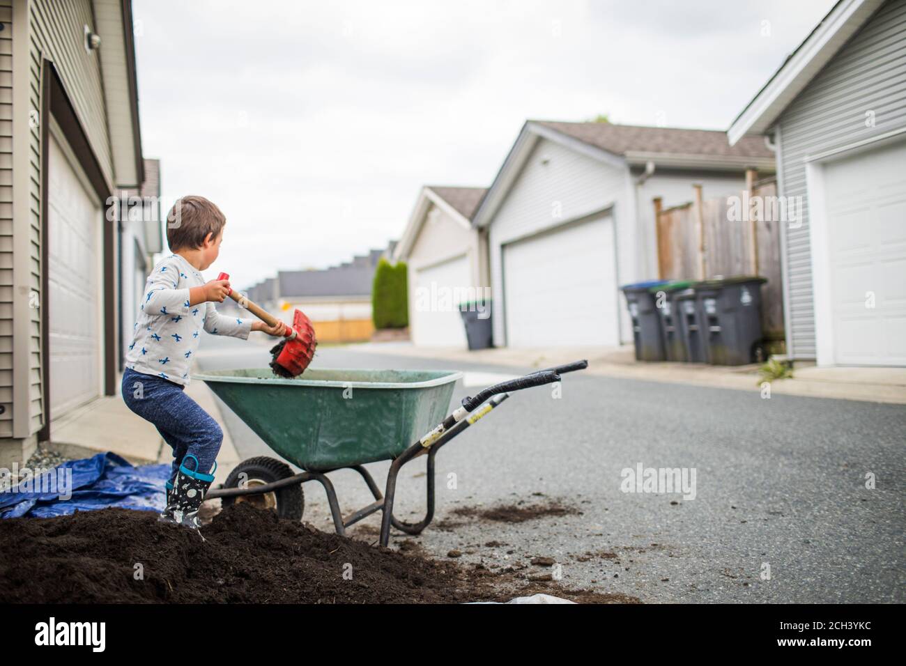 Young boy scooping pile of soil into wheelbarrow in back alley Stock Photo
