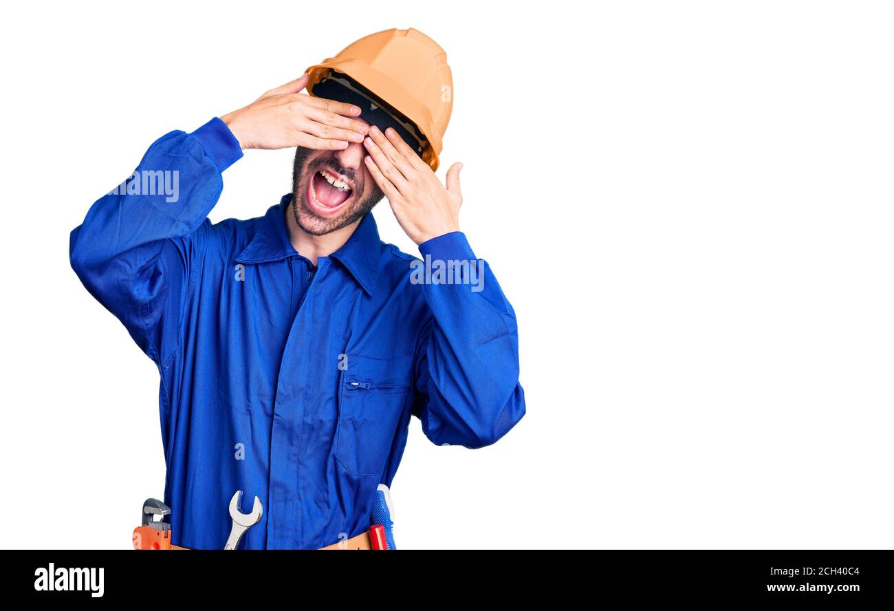 Young hispanic man wearing worker uniform covering eyes with hands ...