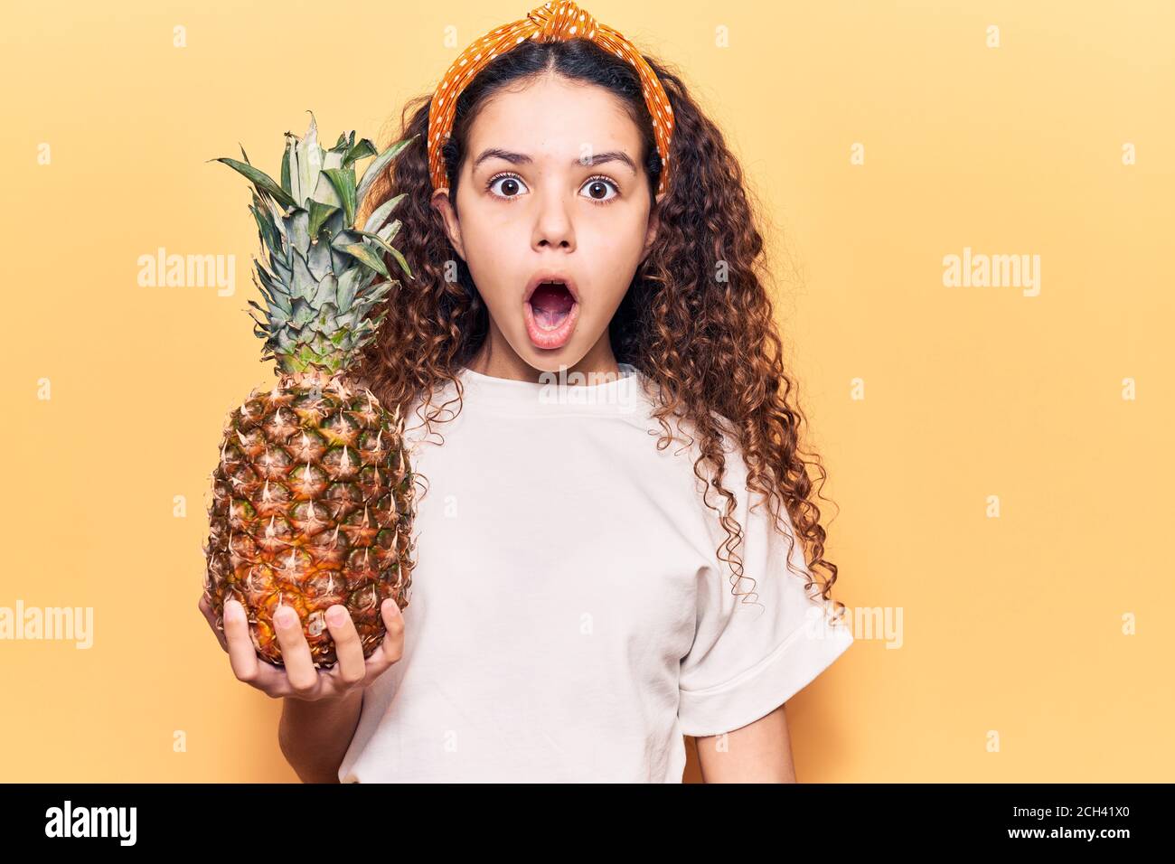 Beautiful kid girl with curly hair holding pineapple scared and amazed with  open mouth for surprise, disbelief face Stock Photo - Alamy