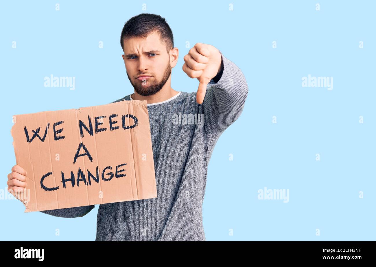 Young handsome man holding we need a change banner with angry face, negative sign showing dislike with thumbs down, rejection concept Stock Photo