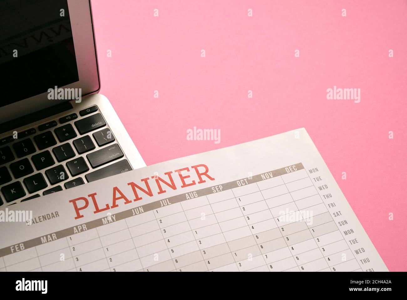 Calendar planner and computer laptop on top of pink table top. Flat lay. Stock Photo