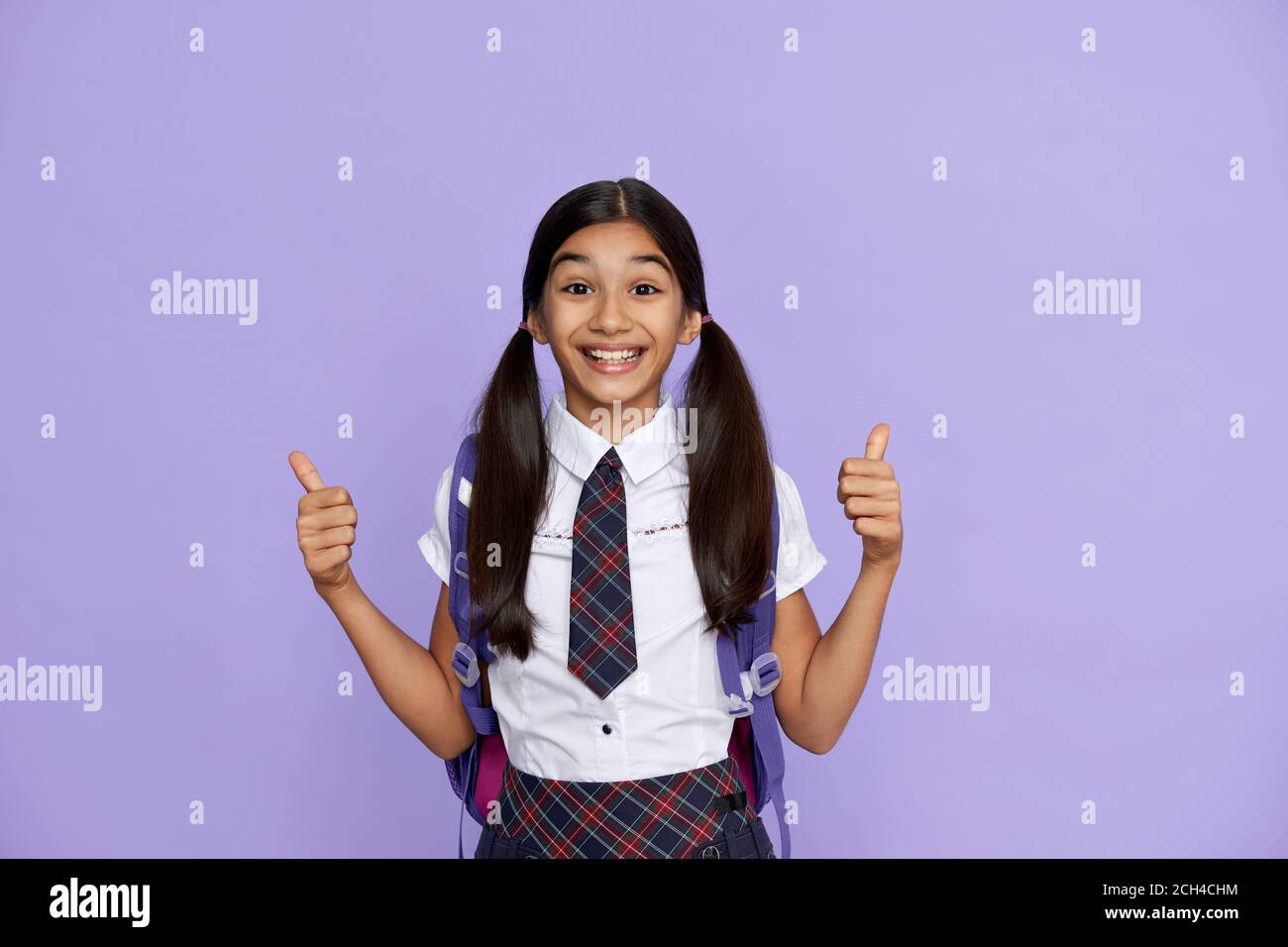 Excited happy indian school girl show thumbs up isolated on violet background. Stock Photo