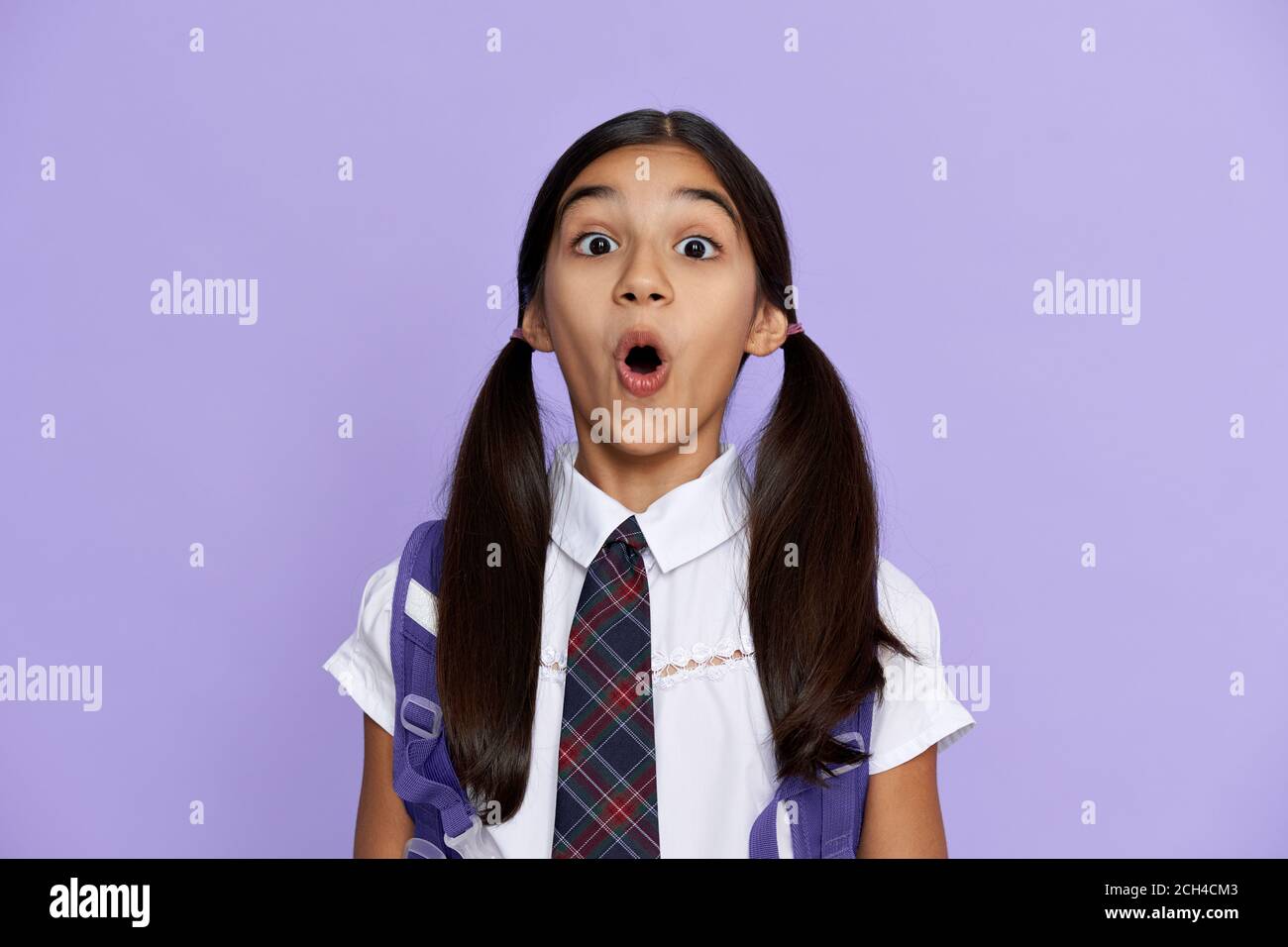 Funny amazed indian school girl looking at camera isolated on violet background. Stock Photo