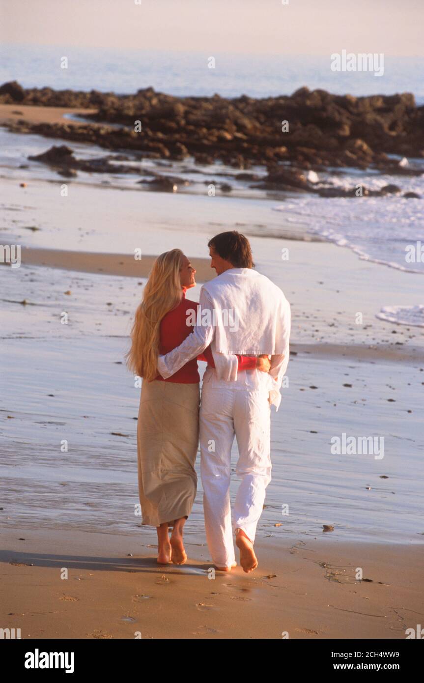 Couple enjoying romantic moments walking on sandy shore along Southern California coast in sunset light Stock Photo