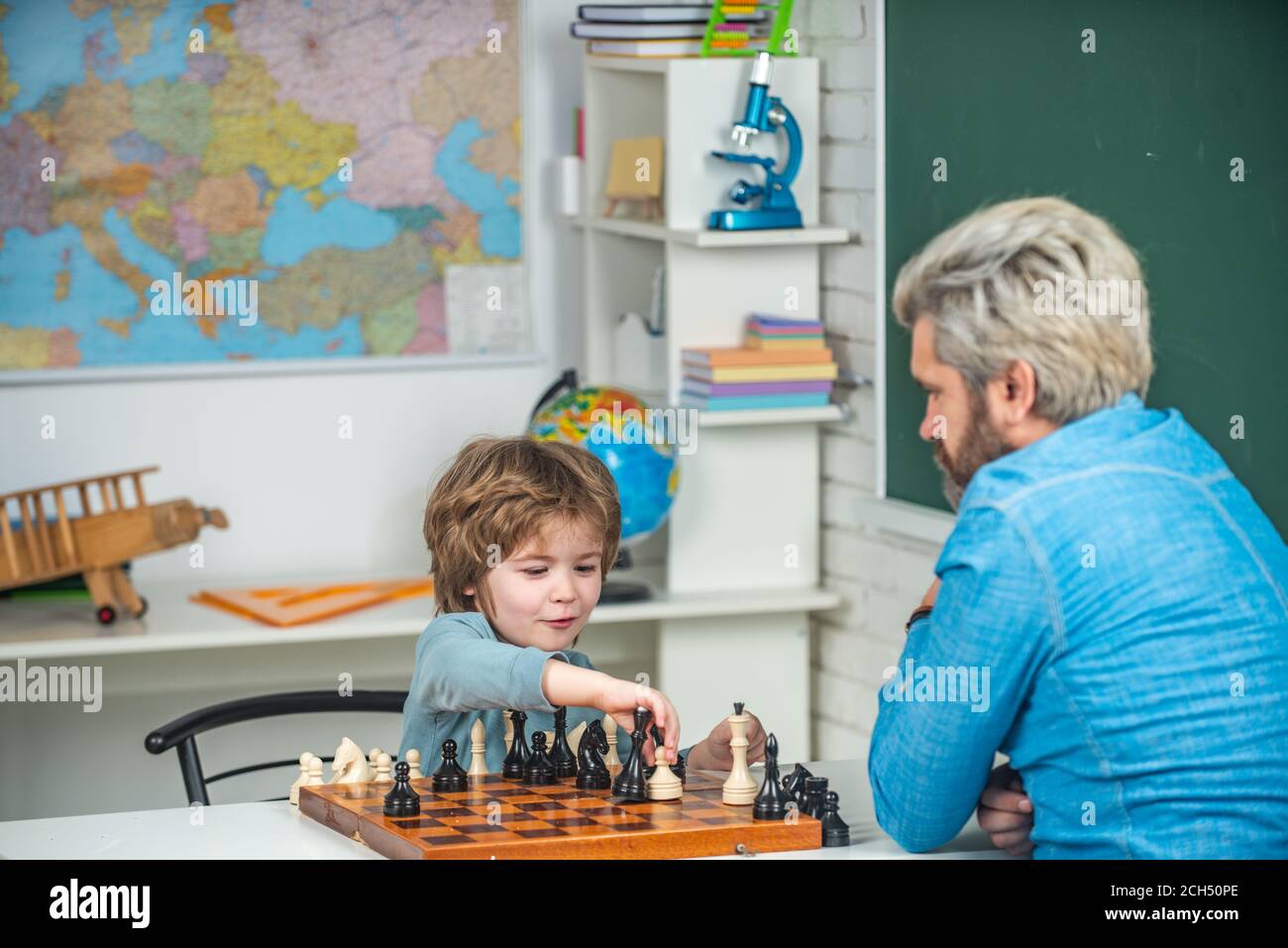 Fathers day. Happy little kid playing chess with senior man at home. Kid Playing Chess. Father and son playing chess. Home tutor helping boy with Stock Photo