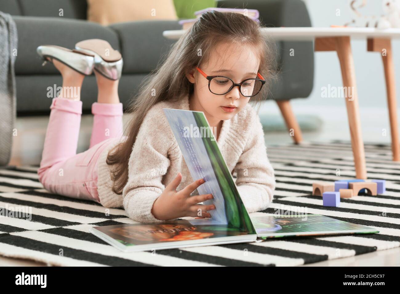 Cute little girl reading book at home Stock Photo - Alamy