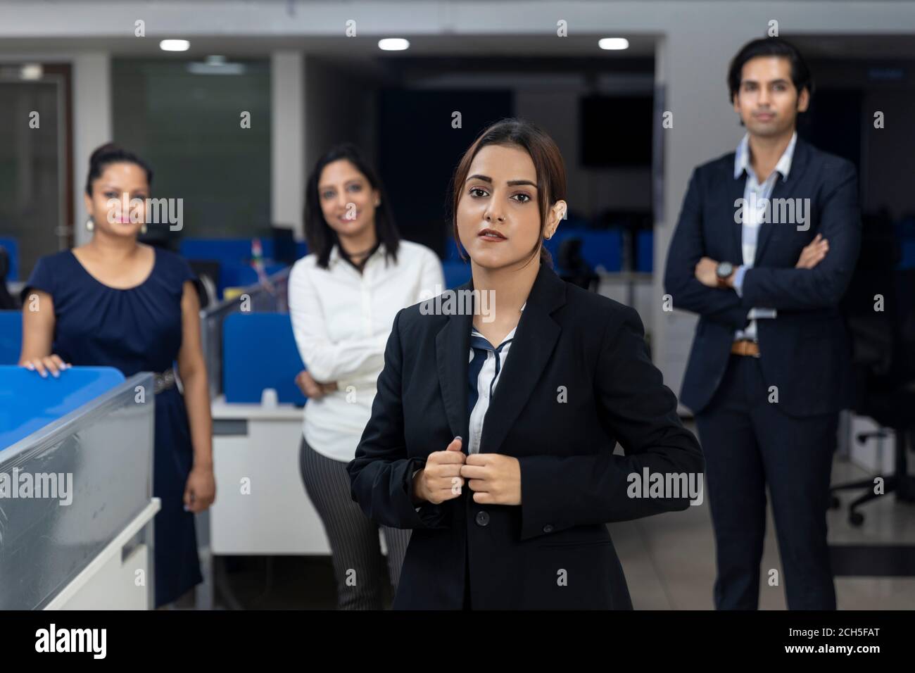Confident Indian businesswoman standing infront of her office colleagues, selective focus, corporate environment, team members, business office. Stock Photo