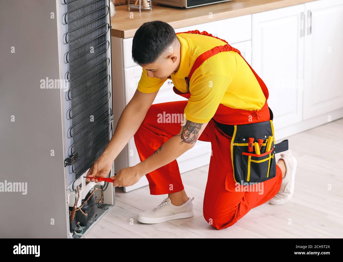 Worker repairing fridge in kitchen Stock Photo