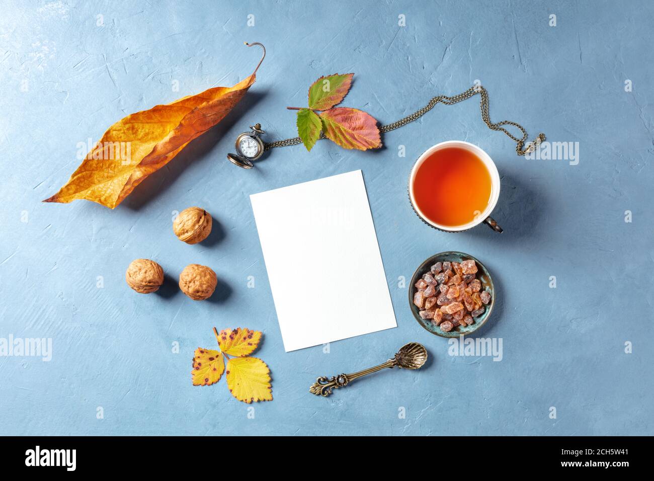 Autumn stationery mockup of an A5 invitation or greeting card, shot from the top with tea and fall leaves, with a vintage watch and nuts Stock Photo