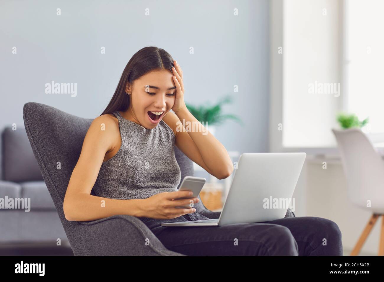 Super happy young girl receiving social media notification sitting in armchair at home Stock Photo