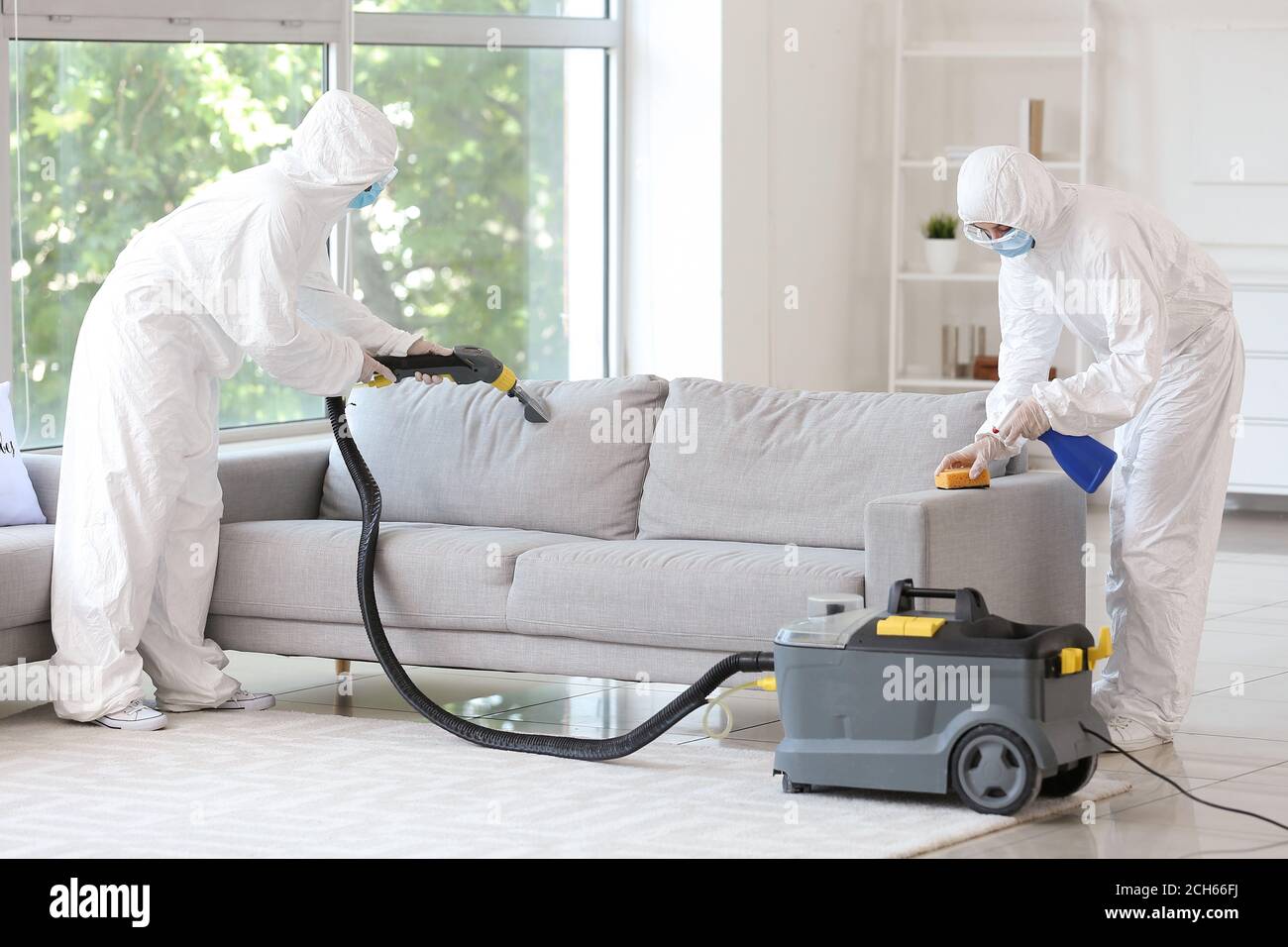 Workers in biohazard costume removing dirt from sofa in house Stock Photo